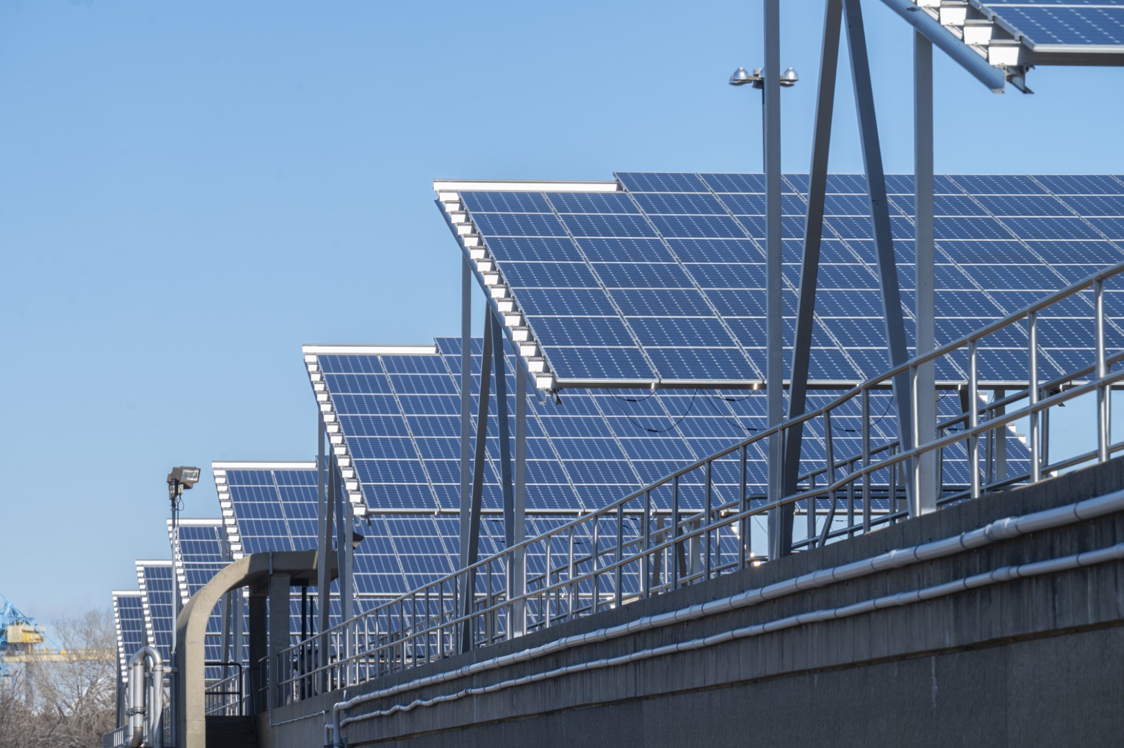Row of solar panels mounted on metal frames above a concrete structure with railings and pipes.